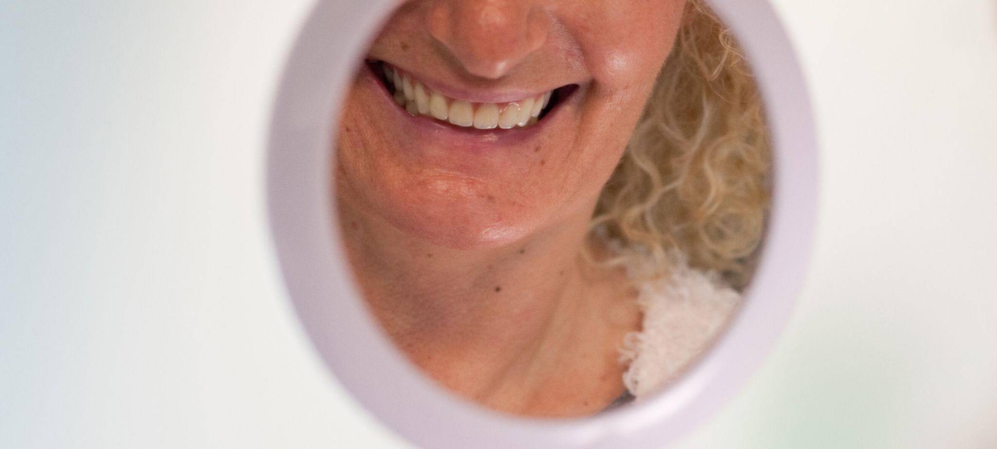 Frau schaut sich ihre Zähne in einem Handspiegel an