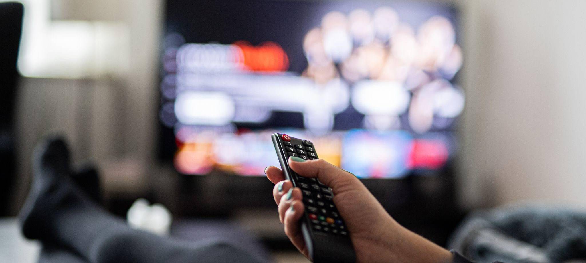Eine Frau sitzt vor dem Fernseher und hält die Fernbedienung