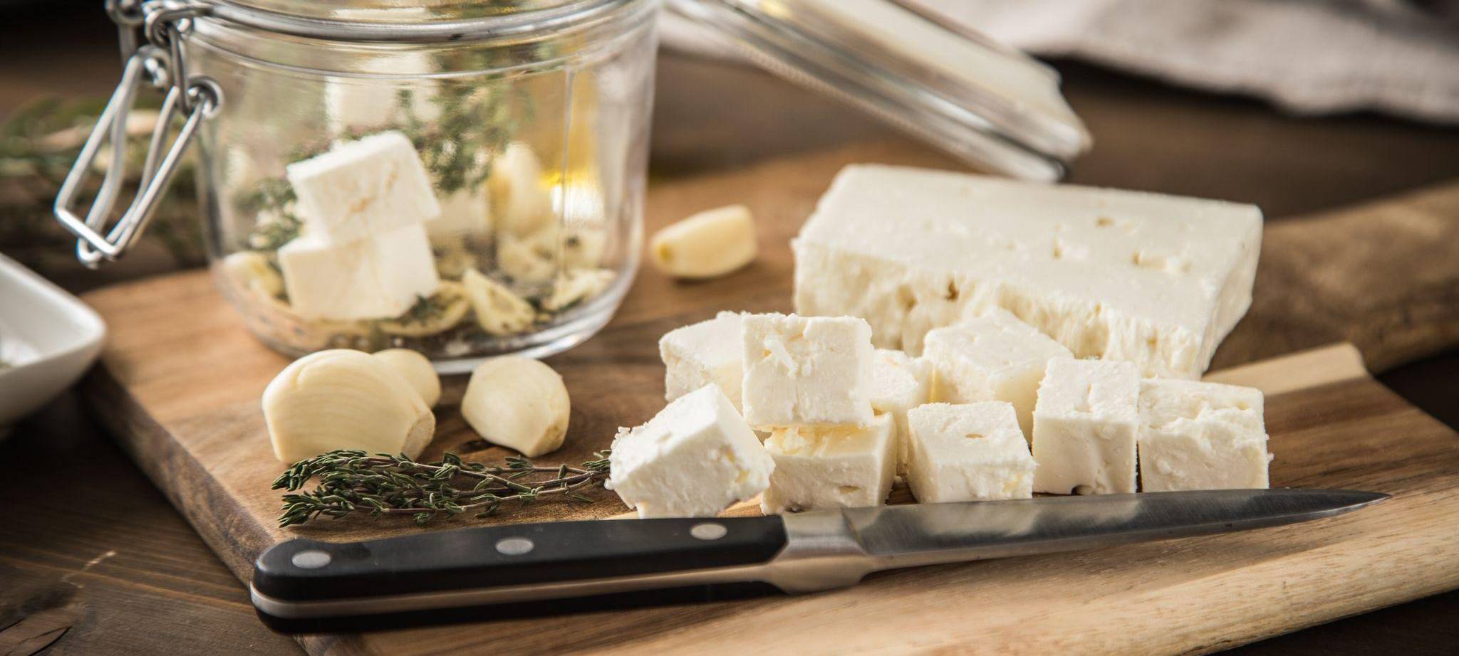 Feta mit Öl, Kräutern und Knoblauch auf einem Holzbrett